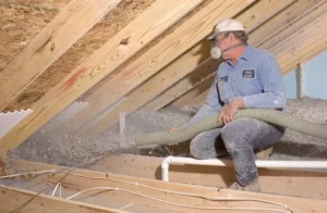 Technician blowing loose-fill cellulose insulation into an unfinished attic.